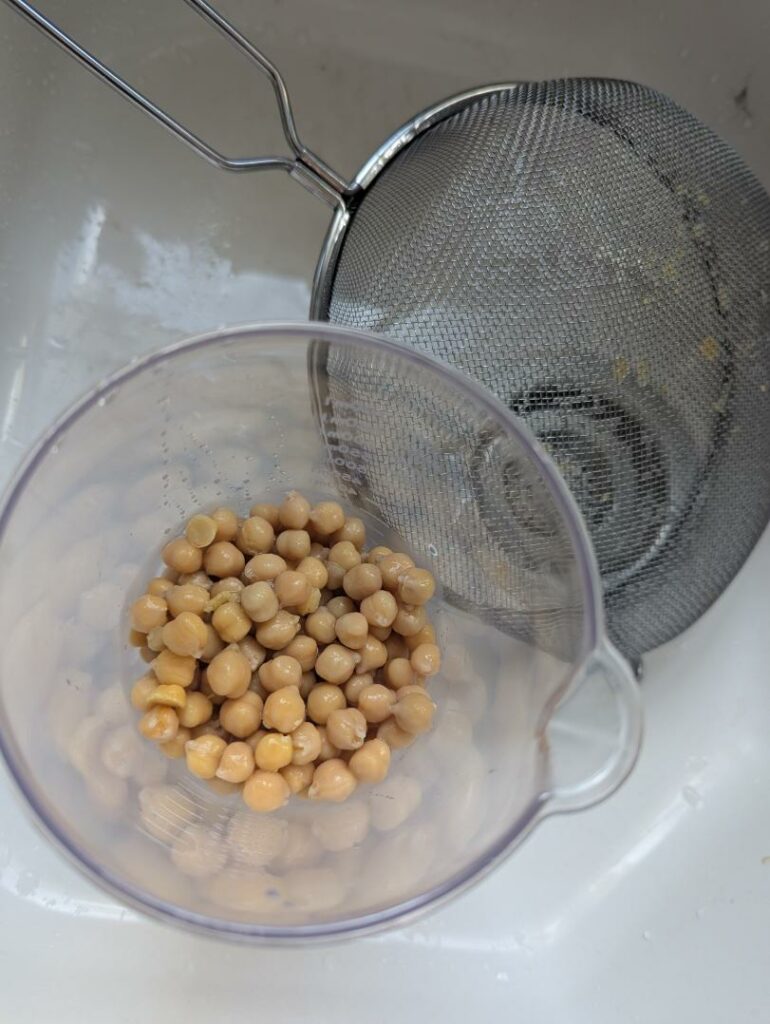 Pois chiches cuits égouttés dans le bol du mixeur, à côté d'une passoire