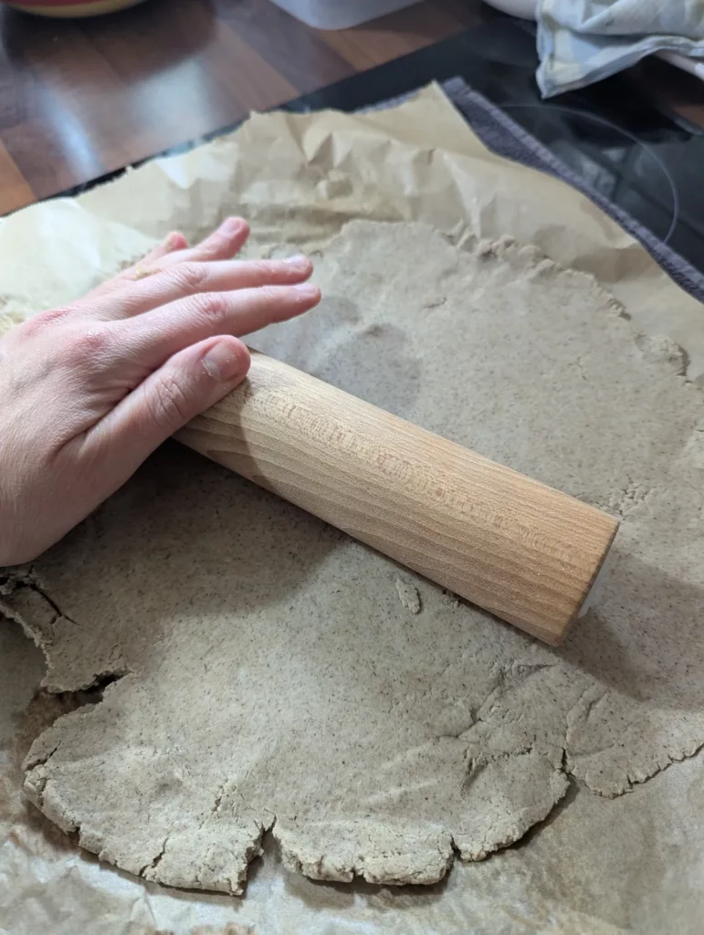 Pâte à pizza sans gluten étalée au rouleau entre deux feuilles de papier cuisson
