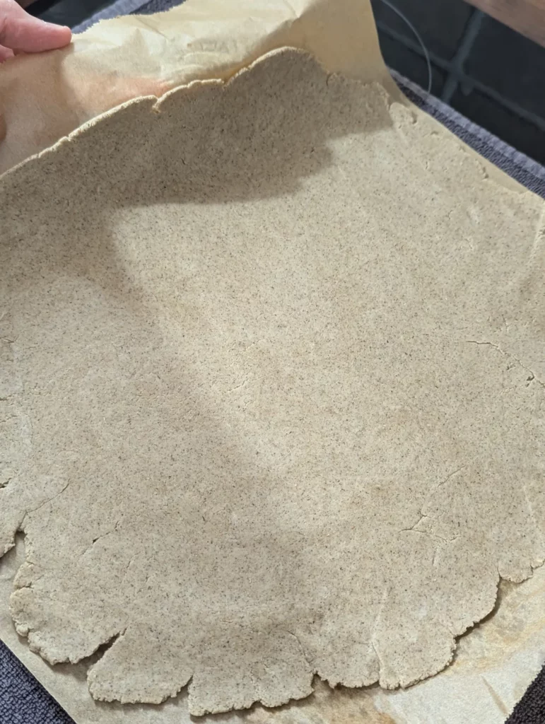 Pâte à pizza sans gluten étalée finement sur papier cuisson