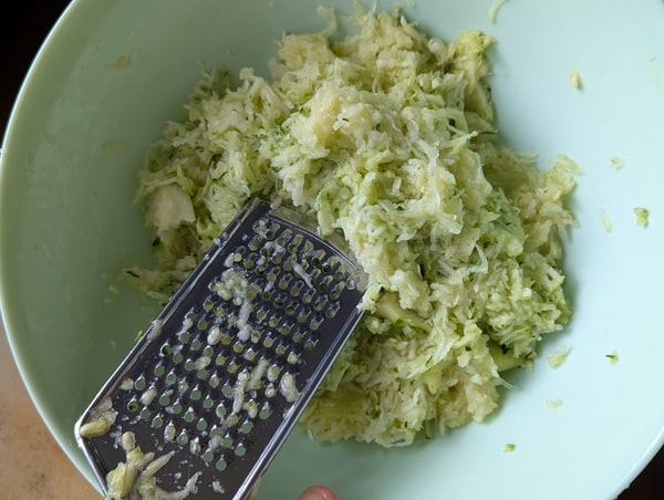 Courgette râpée à gros trous, s’accumulant dans un bol sous une râpe manuelle.