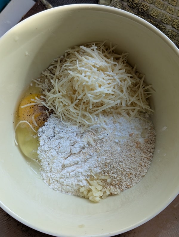 Ingrédients (œuf battu, farine, parmesan, ail, herbes) mélangés dans un grand saladier.