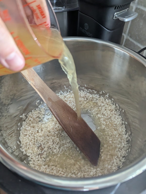 Première louche de bouillon chaud ajoutée au riz, début de la cuisson de ce risotto facile.